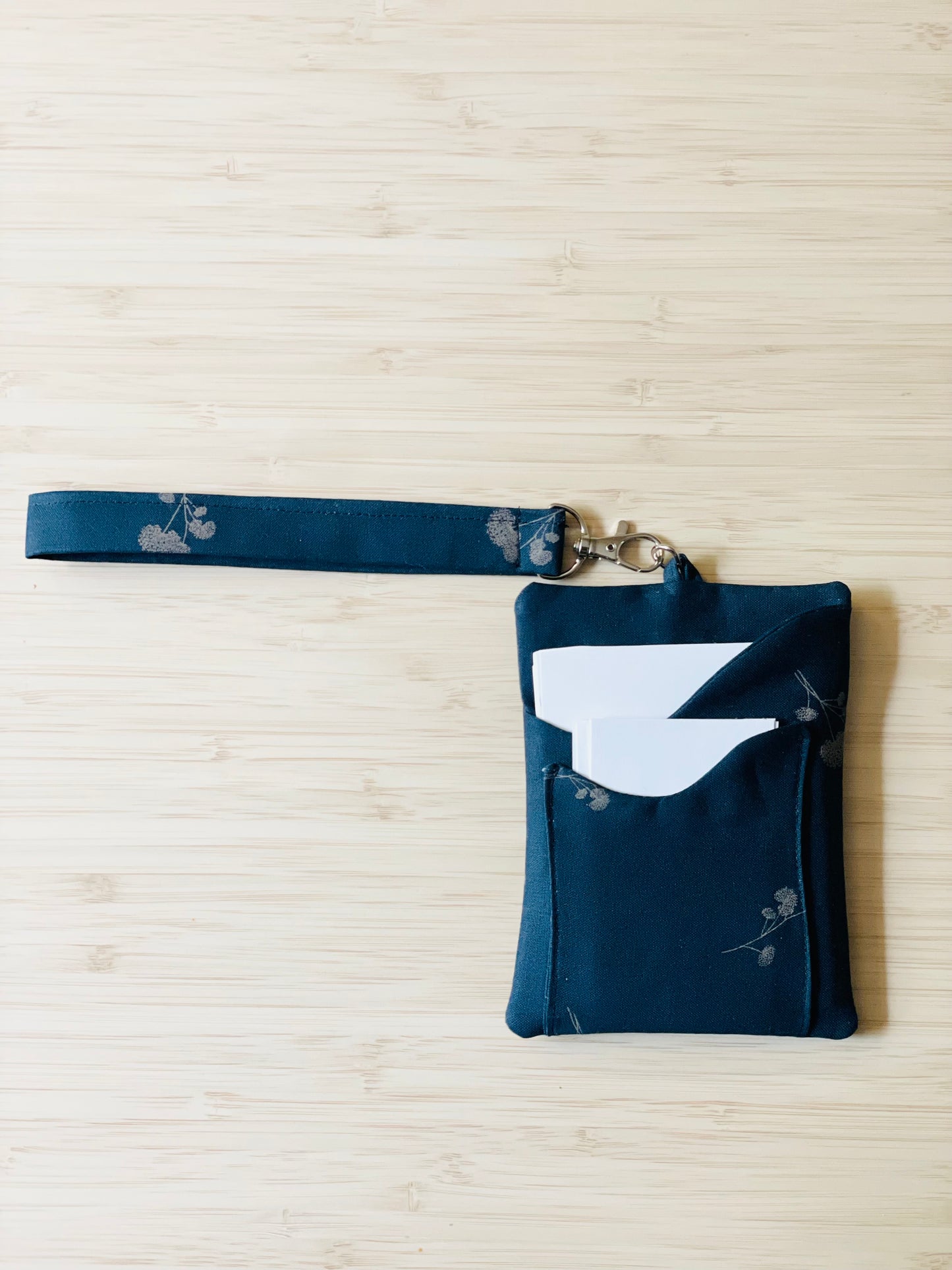 Navy blue pouch with small beige botanical flowers. This is a tract holder with wristlet and crossbody wearing options.