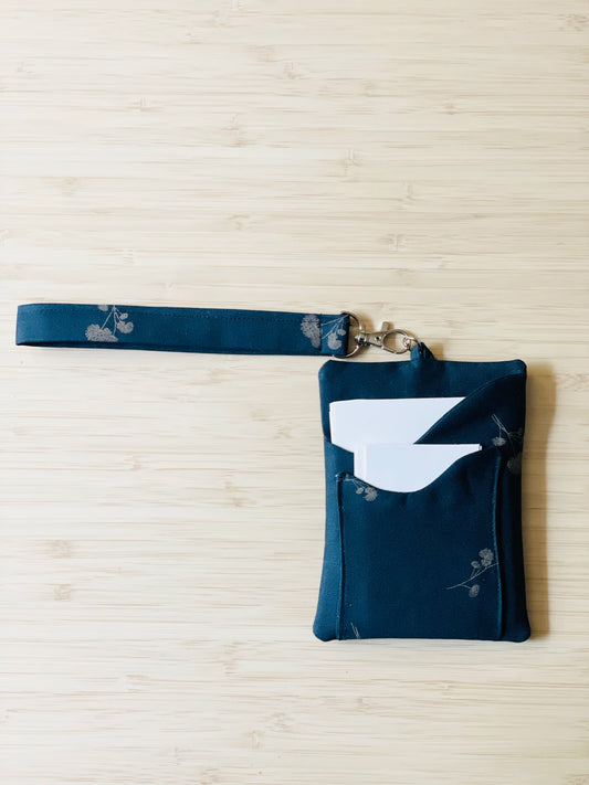 Navy blue pouch with small beige botanical flowers. This is a tract holder with wristlet and crossbody wearing options.